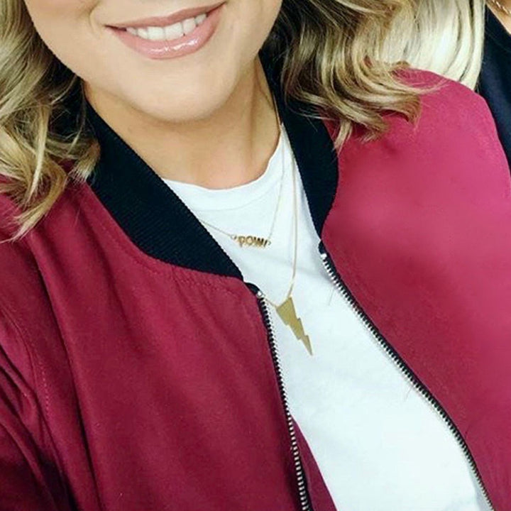 A close-up of a woman wearing a burgundy bomber jacket with a black ribbed collar, layered over a white t-shirt and Edge Only mini pow pendant in 18ct gold vermeil.